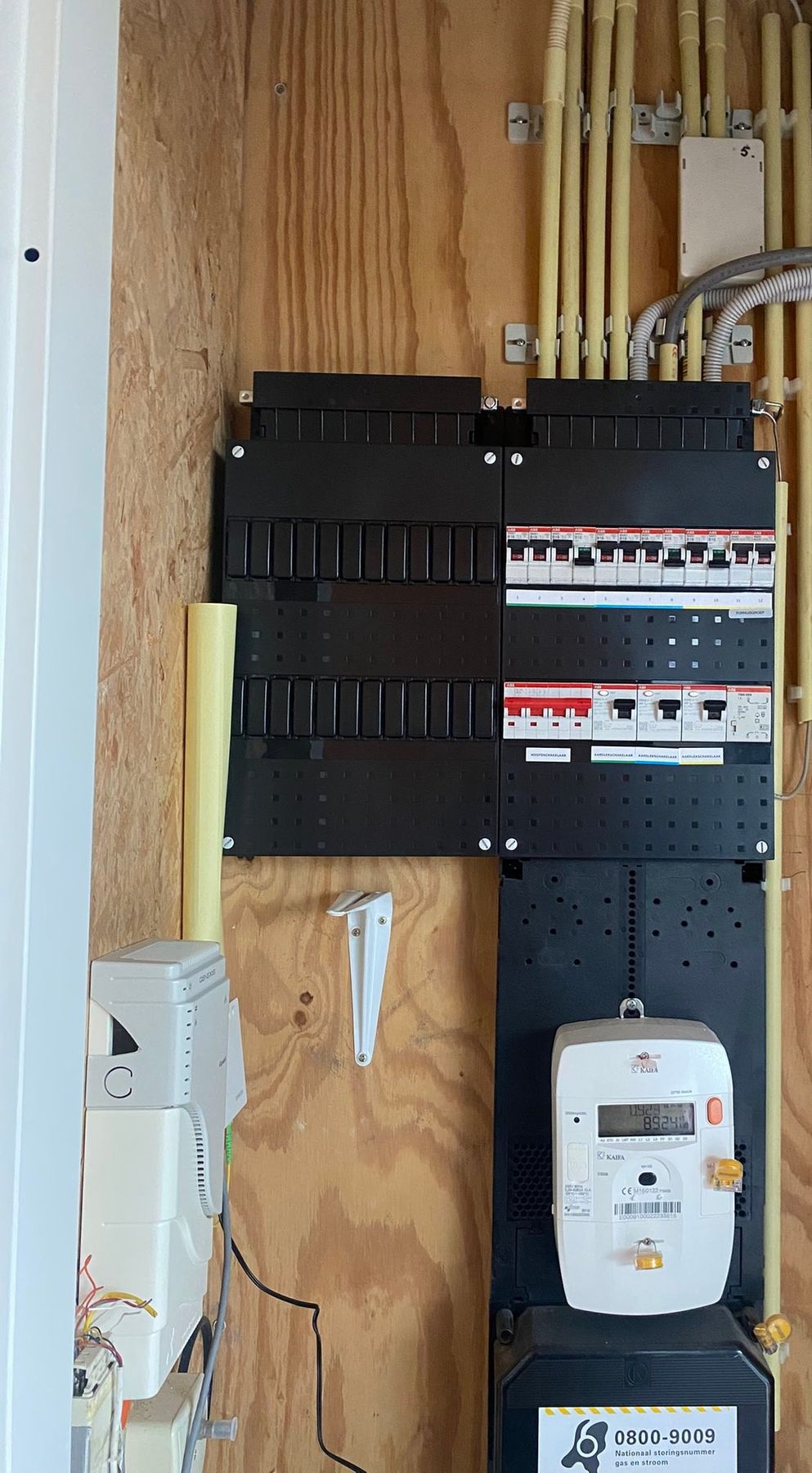 Na: dezelfde meterkast met een nieuwe zwarte groepenkast, twaalf groepen en drie aardlekschakelaars